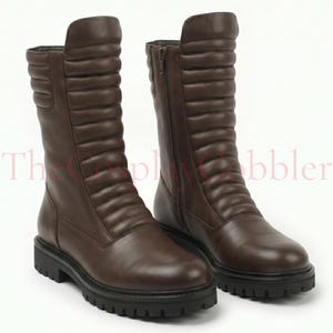 May include: A pair of dark brown mid-calf boots featuring a quilted vertical panel design on the front shaft, a side zip closure, and a thick black lug sole. The text TheCosplayCobbler is visible across the centre of the image.