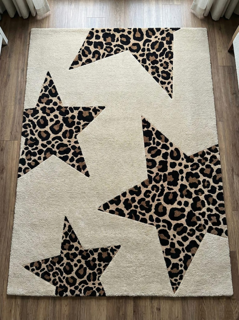 May include: A rectangular area rug with a cream-colored background and four large star shapes. The stars are filled with a brown and black leopard print pattern. The rug is made of a soft, plush material.