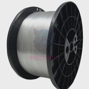 May include: A large spool of silver-colored filament wound tightly around a black plastic reel. The reel features a circular spoke design and a central hub. The word PROTOBIT is printed in red letters on the surface of the silver filament.