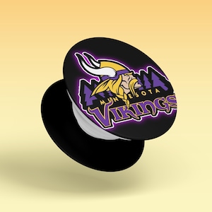 May include: A black circular phone grip featuring the Minnesota Vikings logo, which includes a Viking head with a yellow and purple helmet, and the text Minnesota Vikings in purple and white lettering against a dark background.