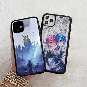 May include: Two phone cases with black borders. One features a blue and gray fantasy scene with a figure and a castle. The other case displays a manga-style illustration of two anime characters with pink and blue hair, set against a comic strip background.