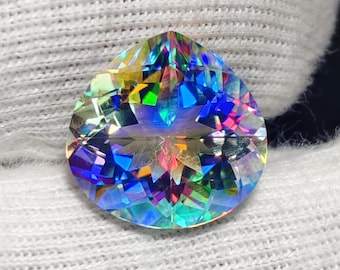 May include: A pear-shaped, faceted gemstone displaying a vibrant, iridescent rainbow spectrum of colors including blue, green, yellow, and pink. The stone features a brilliant cut with sharp geometric reflections across its surface.