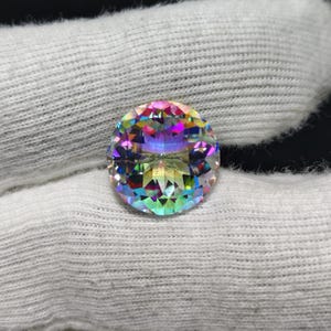 Peut inclure: Une pierre précieuse ronde à facettes affichant un spectre de couleurs arc-en-ciel irisé et vibrant. La pierre présente une taille brillant avec de nombreuses facettes triangulaires qui reflètent la lumière, créant un effet prismatique.