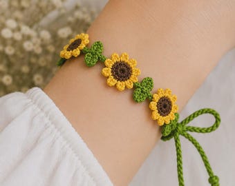 May include: Crocheted bracelet featuring yellow and brown sunflowers with green leaves. The bracelet is tied with a green string and bow. The bracelet is a charming accessory.