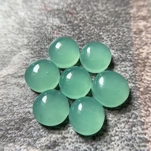 May include: Seven round, polished, light green gemstones arranged in a circular pattern. The stones have a smooth, glossy surface, reflecting light. The gemstones are a soft, muted green color.