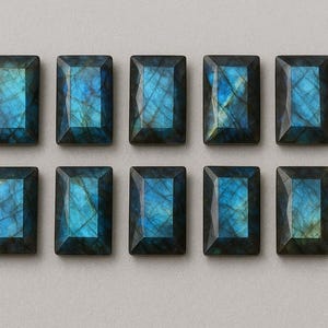 Pode incluir: Dez pedras preciosas retangulares de labradorite com iridescência azul e verde-azulado. Cada pedra tem uma borda cinza escura e está colocada sobre um fundo cinza claro. As pedras estão dispostas em duas fileiras de cinco.