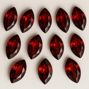 以下が含まれることがあります： 深紅色のマーキス型の宝石が12個並んだ画像。各宝石は光を捉える多面的なカットが施されています。中立的な背景に配置された宝石は、その形と色を際立たせています。