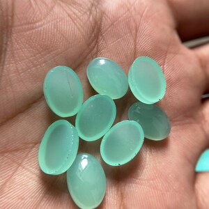 May include: A collection of eight oval-shaped, translucent, light-green gemstones. The stones have a smooth, polished surface and are displayed against a neutral background. These gemstones are ideal for jewelry making.