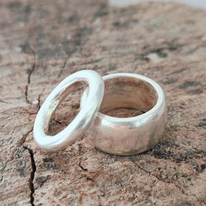 May include: Two silver rings with a polished finish. One ring is thin and narrow, while the other is wider and thicker. The inner band of the thinner ring features a visible 925 hallmark stamp, indicating sterling silver composition.