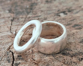 May include: Two silver rings with a polished finish. One ring is thin and narrow, while the other is wider and thicker. The inner band of the thinner ring features a visible 925 hallmark stamp, indicating sterling silver composition.