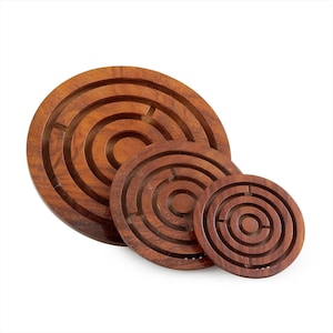 Puede incluir: Tres rompecabezas de laberinto de madera de diferentes tamaños. Los rompecabezas circulares presentan anillos concéntricos que forman caminos de laberinto. La madera tiene un tono marrón rojizo cálido. Los rompecabezas están dispuestos sobre un fondo blanco.
