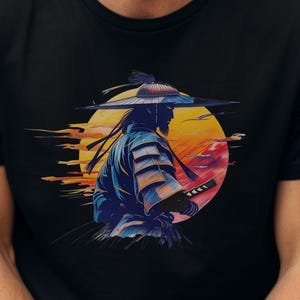 Op de afbeelding: Zwart t-shirt met een afbeelding van een samoerai-krijger met een zwaard, tegen een zonsondergang. De samoerai draagt blauwe en witte kleding en een traditionele hoed. Het ontwerp staat centraal op het shirt.