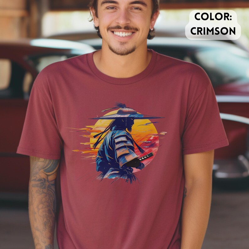 Op de afbeelding: Karmizijnrood T-shirt met een afbeelding van een samoerai-krijger met een zwaard, tegen een gele en oranje zonsondergang. De samoerai is afgebeeld in blauwe en witte kleding. De tekst "COLOR: CRIMSON" staat rechtsboven.