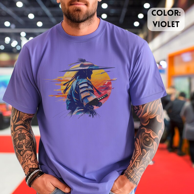 Op de afbeelding: Violet T-shirt met een afbeelding van een samoerai-krijger tegen een gele en rode zonsondergang. De tekst "COLOR: VIOLET" wordt weergegeven in een witte doos. Het shirt is effen violet van kleur. Japans thema.