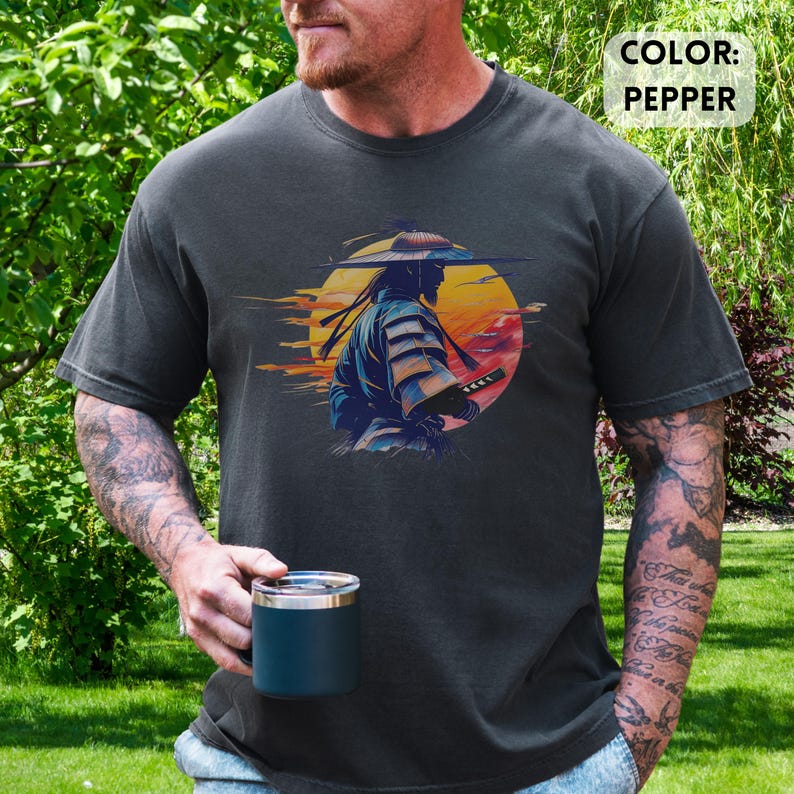 Op de afbeelding: Pepperkleurig t-shirt met een afbeelding van een samoerai-krijger met een zwaard tegen een zonsondergang. Het ontwerp bevat een gele zon en oranje en rode tinten. De tekst "COLOR: PEPPER" staat rechtsboven.