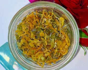 May include: A clear glass jar filled with dried herbs and flowers, with a pink flower, a red rose, and a blue crystal on a white background. The herbs are yellow and green.