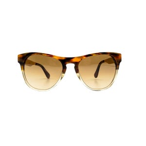 May include: Sunglasses with a tortoiseshell pattern frame and gradient brown lenses. The frame has a rounded shape with a clear lower rim. The arms are dark brown.