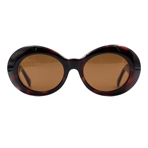 May include: Oval sunglasses with a tortoiseshell pattern frame and brown lenses. The sunglasses have a classic design, suitable for various face shapes. The frame features a dark brown and amber colour combination.