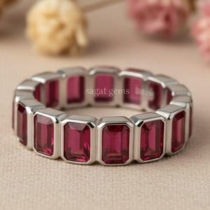 May include: A silver ring with rectangular, deep red gemstones. The ring features a continuous band of stones, creating a bold and elegant design. The brand name "sagat gems" is visible on the ring.