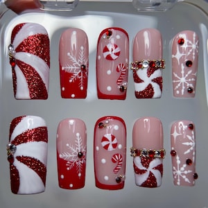 May include: A set of ten artificial nails with a Christmas theme. Designs include red glitter and white swirl patterns, snowflakes, candy canes, and red and white peppermint candies. Some nails have decorative rhinestones.