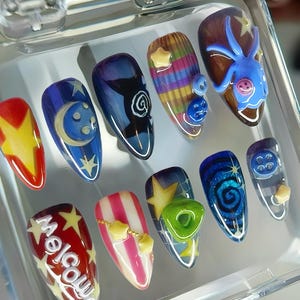 May include: A set of ten artificial nails with various designs. The nails feature a range of colors, including red, yellow, blue, and white, with designs such as stars, moons, swirls, and the word "Welcome".