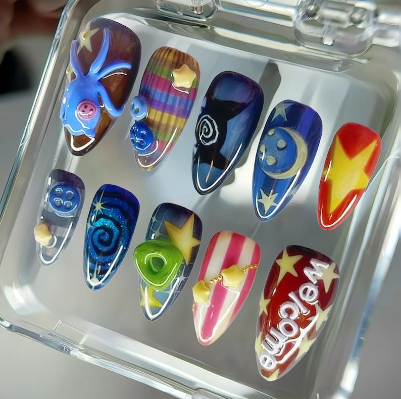 May include: A set of ten artificial nails with various designs. The nails feature a variety of colors, including blue, red, yellow, and white, with designs such as stars, moons, and the word "Welcome". Some nails have 3D embellishments.