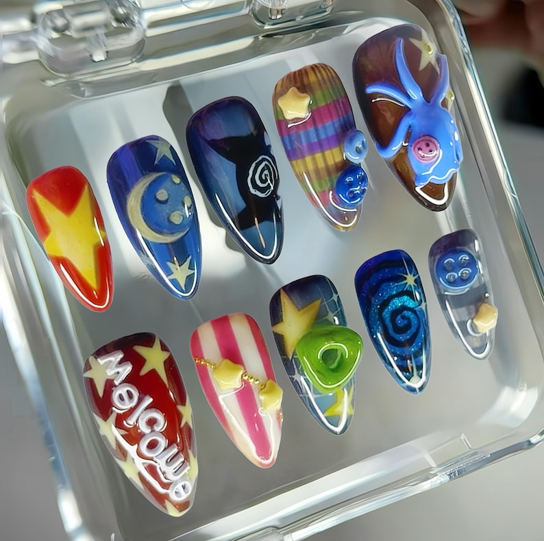 May include: A set of ten artificial nails with various designs. The nails feature a range of colors, including red, yellow, blue, and white, with designs such as stars, moons, swirls, and the word "Welcome".