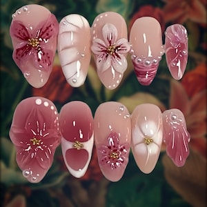 May include: A set of ten artificial nails with a floral theme. The nails are painted in shades of pink and nude, with 3D flower and pearl accents. Some nails feature a heart design. The overall effect is delicate and feminine.