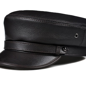 Może przedstawiać: Czarna skórzana czapka z krótkim daszkiem i paskiem. Czapka ma strukturalną koronę i dwa małe metalowe oczka z boku. Klasyczny dodatek do różnych stylizacji.