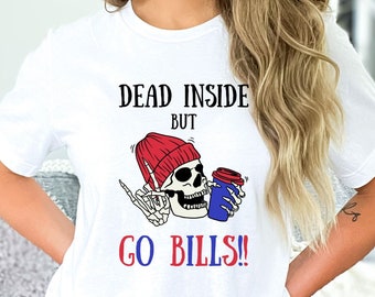 May include: White t-shirt with a graphic of a skeleton wearing a red beanie and holding a coffee cup. Text reads "DEAD INSIDE BUT GO BILLS!!" and "Trellies Boutique".
