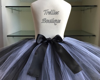 May include: A black and white tulle tutu skirt with a black satin ribbon tied around the waist. The skirt is on a white mannequin. The text "Trellis Boutique" is written on the mannequin's torso.