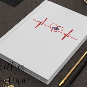 May include: White notebook with a red heartbeat graphic and a purple buffalo silhouette inside a red heart. The notebook has the text "Trellis Boutique" on the bottom left corner.