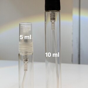 Pu&ograve; includere: Due atomizzatori di profumo in vetro trasparente, uno con l'etichetta "5 ml" e l'altro "10 ml". Gli atomizzatori hanno un corpo in vetro trasparente, un nebulizzatore e un tappo nero. Lo sfondo &egrave; di colore chiaro e neutro.