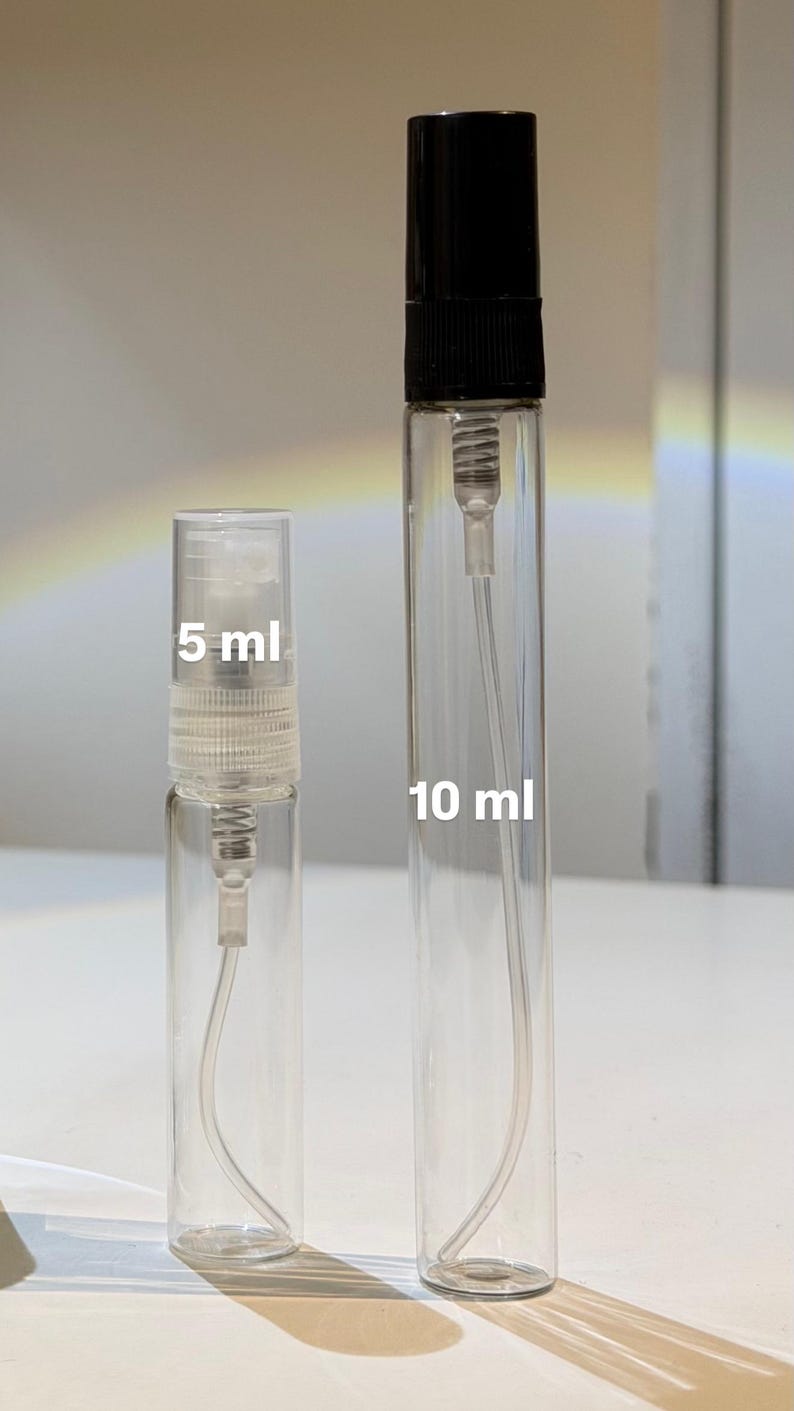 Pu&ograve; includere: Due atomizzatori di profumo in vetro trasparente, uno con l'etichetta "5 ml" e l'altro "10 ml". Gli atomizzatori hanno un corpo in vetro trasparente, un nebulizzatore e un tappo nero. Lo sfondo &egrave; di colore chiaro e neutro.