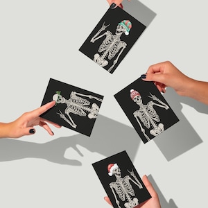 Può includere: Quattro cartoline rettangolari con sfondo nero e illustrazioni di scheletri bianchi. Ogni scheletro indossa un diverso accessorio natalizio, tra cui un cappello da Babbo Natale, un cappello da elfo verde, un berretto di lana rosso e occhiali festivi verdi.