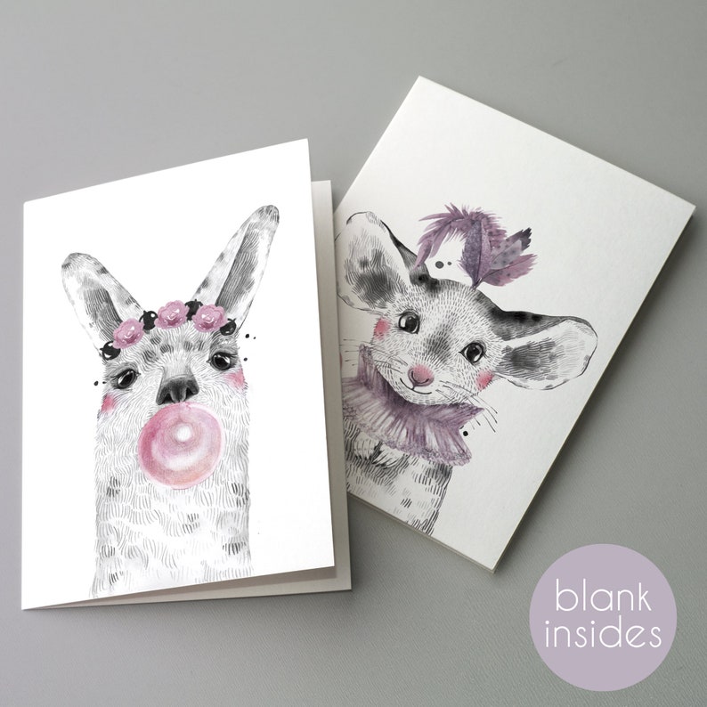 May include: Two blank greeting cards with watercolour illustrations. One card features a llama blowing a bubblegum bubble and wearing a floral crown. The other card shows a mouse with a purple collar and feather. The cards are blank inside.
