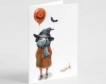 May include: A white greeting card featuring a watercolor illustration of a figure wearing a dark witch hat, a brown coat, and a blue scarf. The figure holds an orange jack-o'-lantern balloon, with a small black bat nearby and the word mood.