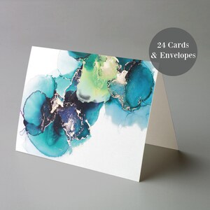 a white card with a colorful abstract design, including shades of blue, green, and gold. The card is displayed on a gray surface, and there is a text overlay that reads "24 Cards & Envelopes".