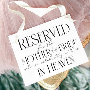 May include: White sign with black text that reads "RESERVED for the MOTHER of the BRIDE who is celebrating with us IN HEAVEN".