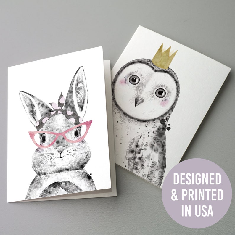 May include: Two greeting cards with watercolour animal illustrations. One card shows a rabbit wearing pink glasses and a headband. The other depicts an owl with a gold crown. The cards are printed in the USA.