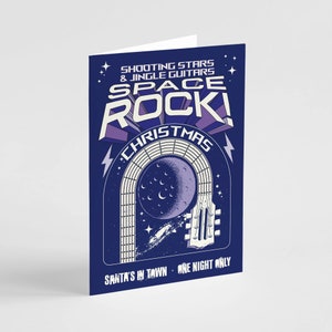 May include: A folded greeting card with a dark blue background. The card features the words "SPACE ROCK! CHRISTMAS" in white and purple, with a guitar illustration and a moon. The text "SHOOTING STARS & JINGLE GUITARS" and "SANTA'S IN TOWN - ONE NIGHT ONLY" are also visible.