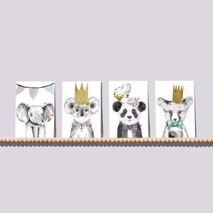 May include: Four watercolour animal prints displayed on a wooden shelf. The prints depict an elephant, koala, panda, and fox, each wearing a crown and bow tie or collar. The elephant has a banner in the background. The panda has a floral crown.