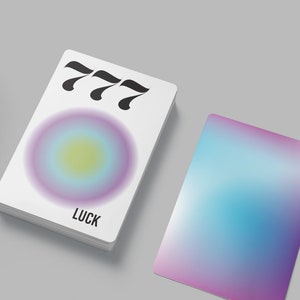 May include: A white card with the number 777 printed in black. The card has a gradient circle in shades of purple, blue, and yellow. The word "LUCK" is printed in black at the bottom of the card.