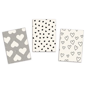 May include: Three rectangular cards with heart patterns. One card has a black and white polka dot background with large white hearts. Another has a cream background with small black hearts. The third card has a cream background with black outline hearts.