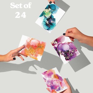 four hands holding up colorful abstract art cards against a light background.