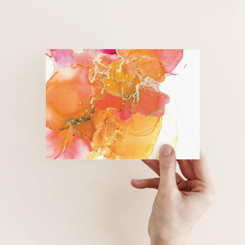 A hand is holding up a piece of paper with an abstract, colorful painting of flowers or flowers in a liquid medium.