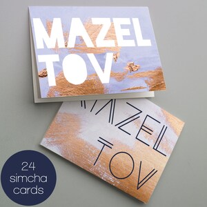 May include: A set of 24 blank greeting cards with a gold and blue abstract design. The cards feature the text "Mazel Tov" in white and black lettering.