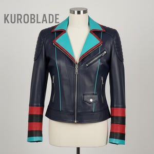 Puede incluir: Chaqueta de cuero azul marino con cuello turquesa y ribete rojo. La chaqueta tiene cierre de cremallera, bolsillos laterales y puños a rayas rojas y negras. El texto "KUROBLADE" es visible en la esquina superior izquierda.