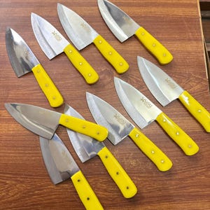 Könnte beinhalten: Eine Sammlung von zehn Küchenmessern aus Edelstahl mit leuchtend gelben Griffen. Die Klingen sind silberfarben und die Griffe sind einfarbig gelb. Die Messer sind auf einer Holzoberfläche angeordnet.