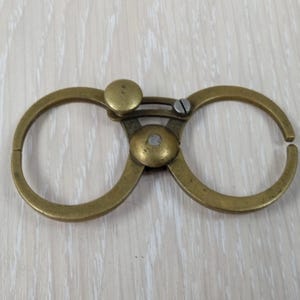 以下が含まれることがあります： 中央のピボット機構で接続された2つの円形リングを備えた真鍮製のキャリパーツール。上部には小さなローレット加工された調整ノブと平頭ねじがあり、2つのリングを互いに調整できるようになっています。